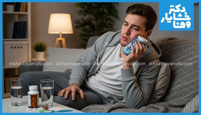 این تصویر مراقبتهای پس از جراحی دندان عقل را نشان میدهد. مردی روی کاناپه نشسته و برای کاهش تورم و درد، از کمپرس یخ روی گونهاش استفاده میکند. دارو و نوشیدنی نیز در کنار او قرار دارد.