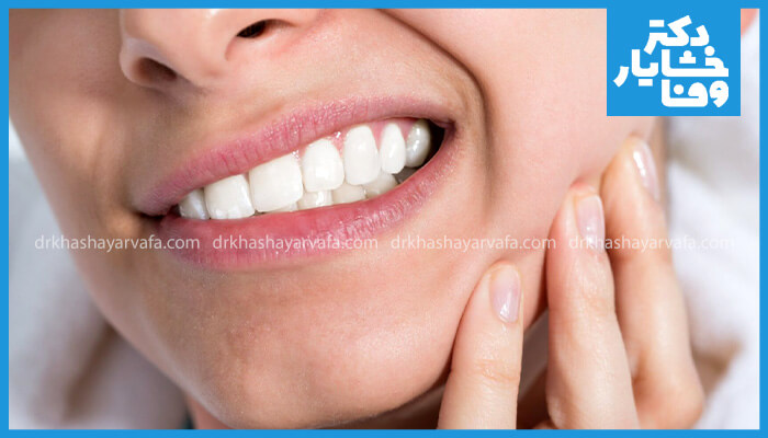 تصویری از یک فرد که به دلیل حساسیت دندانی پس از انجام روش‌های دندانپزشکی، گونه خود را گرفته است.