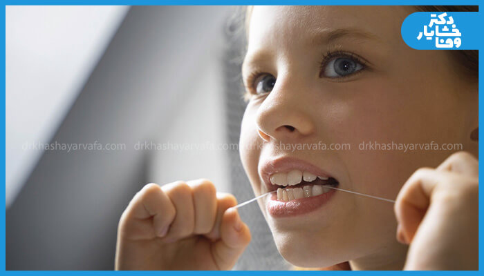 تصویری از یک کودک در حال نخ دندان کشیدن برای تمیز کردن دندان‌ها
