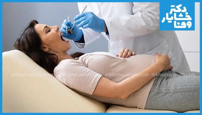  زن باردار درازکشیده روی صندلی دندانپزشکی در حال معاینه دهان.