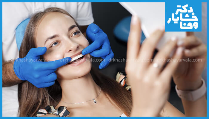 دندانپزشک در حال بررسی و معاینه دندان‌های بیمار زن پس از اتمام جرم‌گیری برای اطمینان از سلامت لثه‌ها و رضایت از نتیجه.